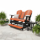 The Kanyon Living Poly Lumber 5′ Adirondack Glider Tall Version in orange and black features comfy beige pillows. This inviting bench sits on a patio with potted ferns, flowers, and a side table holding a mug and book.