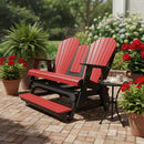 The Kanyon Living Poly Lumber 5′ Adirondack Glider Tall Version in Red and Black sits on a brick patio with potted red flowers and a green fern nearby, while a black side table holds a cup and saucer for outdoor relaxation.