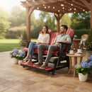 A couple relaxes and smiles on the Kanyon Living Poly Lumber 5′ Adirondack Glider Tall Version in red and black under a pergola, surrounded by potted hydrangeas, coffee cups, string lights, and a lush garden—perfect for outdoor seating.
