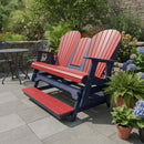 The Kanyon Living Poly Lumber 5′ Adirondack Glider Tall Version in red and blue sits on a stone patio, surrounded by green plants, potted flowers, a metal table and chairs, with a stone wall and trees in the background.