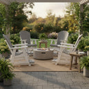 A cozy patio features four Kanyon Living Poly Lumber Adirondack Glider Chair Tall Deluxe in Driftwood Grey and White, arranged around a circular fire pit beneath a pergola, surrounded by lush greenery on a stone-paved surface.