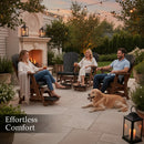 Three people relax in Kanyon Living Poly Lumber Adirondack Glider Chairs (Tall Black & Deluxe Antique Mahogany) by a fire at sunset, a golden retriever nearby and string lights overhead. Text reads, “Effortless Comfort.”.