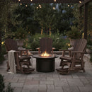 Four Kanyon Living Poly Lumber Adirondack Glider Chairs in Tall Deluxe Brazilian Walnut and Weathered Wood encircle a fire pit on a stone patio under string lights, with lush greenery and a light blanket draped over one chair.