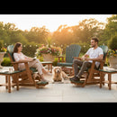 A woman and a man relax and chat on Kanyon Living Poly Lumber Adirondack Glider Chairs (Tall, Dark Green/Cedar Wood) on their patio. A golden retriever rests between them among potted flowers, trees, and sunlight.
