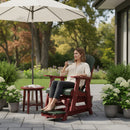 A woman relaxes on a Kanyon Living Poly Lumber Adirondack Glider Chair Tall in Dark Green and Cherry Wood, sipping coffee under a large umbrella, surrounded by flowers and greenery on the patio, with trees and a house behind her.