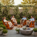Four adults relax and chat in Kanyon Living Poly Lumber Adirondack Glider Chairs (Tall, Dark Wood & Orange) on a patio by a fire pit. A golden retriever rests nearby, with flowering plants and greenery enhancing the inviting scene.