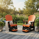 Two Kanyon Living Poly Lumber Adirondack Glider Chair Talls in orange and black sit with cushions and pillows on a round rug atop a wooden deck, surrounded by plants, flowers, lanterns, and trees. A small table with a book is set between them.