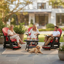 Three adults relax outdoors on Kanyon Living Poly Lumber Adirondack Glider Chair Tall Red and Black, chatting around a small table. A golden retriever lies on a rug nearby, with string lights above and a house in the background.
