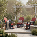Three red and navy Adirondack chairs with cushions and pillows surround a fire pit on a stone patio. A pergola with climbing roses and lush garden plants create a cozy, inviting outdoor setting.