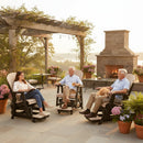 Three people relax on Kanyon Living Poly Lumber Adirondack Glider Chair Tall in Seashell and Black near an outdoor fireplace, one with a dog. Potted flowers, a pergola, and scenic views showcase this Amish crafted Kanyon Living furniture set.