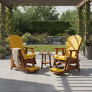 Two Kanyon Living Poly Lumber Adirondack Glider Chairs in Tall Yellow and Cedar Wood are on a patio beneath a pergola, facing a small round table with cups. A blanket is draped over one chair, with garden greenery and a fountain visible in the background.