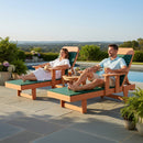 A woman and a man relax on Kanyon Living Poly Lumber Chaise Lounges with Arms in Dark Green and Cedar Wood, enjoying drinks among potted plants as a scenic outdoor view enhances their experience.