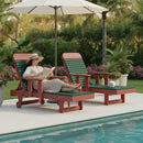 A woman lounges by the pool on the Kanyon Living Poly Lumber Chaise Lounge with Arms in Dark Green and Cherry Wood, wearing sunglasses and a hat. Surrounded by drinks, a towel, and lush plants, she enjoys eco-friendly patio furniture from Kanyon Living.