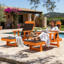 A woman in a white robe reads by the pool on a Kanyon Living Poly Lumber Chaise Lounge with Arms in Dark Wood and Orange. An empty matching chair with a blanket is beside her, set against a Mediterranean-style villa and lush greenery.