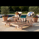 A woman in a hat and light clothes relaxes on the Kanyon Living Poly Lumber Chaise Lounge with Arms Deluxe Brazilian Walnut and Weathered Wood poolside, reading. An empty matching lounge with a blue and white striped towel sits beside her amid potted plants.