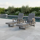 Two Kanyon Living Poly Lumber Chaise Lounges with Arms in Deluxe Driftwood Grey sit poolside on a stone patio, accessorized with a towel, magazine, and sun hat. Lush greenery forms the backdrop for this inviting outdoor relaxation scene.