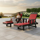 A woman in a white dress relaxes poolside on the Kanyon Living Poly Lumber Chaise Lounge with Arms in red and black, reading a tablet. An identical lounge and small table are beside her, surrounded by greenery and scenic views.