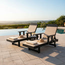 Two Kanyon Living Poly Lumber Chaise Lounges with Arms in Seashell and Black sit poolside under a clear sky, overlooking a scenic landscape. A small table with drinks sits between the brand’s handcrafted outdoor chairs.