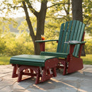 A Kanyon Living Poly Lumber Gliding Ottoman in dark green and cherry wood sits by an Adirondack chair on a stone patio. A drink and magazine rest nearby, while lush trees and sunlight complete this peaceful outdoor setting.