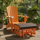 A Kanyon Living Poly Lumber Gliding Ottoman in dark wood and orange sits on a wooden deck with matching Adirondack chair, surrounded by potted plants. A cup and open book rest on the arm, sunlight streaming through the trees.