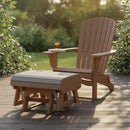 A Kanyon Living Poly Lumber Gliding Ottoman in Light Grey and Weathered Wood sits on a sunlit deck beside an Adirondack chair, surrounded by green bushes, evoking a peaceful and relaxing outdoor furniture scene.