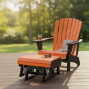 A Kanyon Living Poly Lumber Gliding Ottoman in orange and black complements an Adirondack chair on a wooden deck. A folded gray blanket, sunglasses, and a glass of iced tea rest on the chair, with blurred trees and grass in the background.