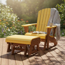 A Kanyon Living Poly Lumber Gliding Ottoman in yellow and cedar wood sits on a wooden deck, topped with a gray blanket. An open book and coffee mug rest nearby, while sunlit garden flowers bloom in the background.