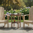 Two wooden Adirondack chairs sit on a stone patio beside the Kanyon Living Poly Lumber Tall Oval Side Table Deluxe in Brazilian Walnut and Weathered Wood. A mug, an open book, and iced tea rest atop it, backed by lush shrubs and blooming hydrangeas.