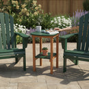 Two green outdoor chairs and a Kanyon Living Poly Lumber Tall Oval Side Table in dark green and cedar wood rest on a stone patio. A hand touches an open book beside a steaming mug and eyeglasses, with flowers and greenery in the background.