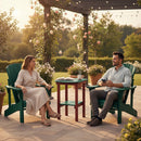 A woman and man sit in green chairs under a pergola, talking and smiling in a sunlit garden. A book and coffee cup rest on the Kanyon Living Poly Lumber Tall Oval Side Table (Dark Green/Cherry Wood), surrounded by potted plants and flowers.