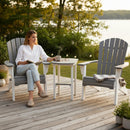 A woman sits reading with coffee on a patio, beside an empty chair and the Kanyon Living Poly Lumber Tall Oval Side Table Deluxe in Driftwood Grey and White by Kanyon Living, with glasses and another cup on the table, overlooking a lake and trees.