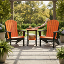 Two bright orange Adirondack chairs sit on a stone patio with the Kanyon Living Poly Lumber Tall Oval Side Table in Orange and Black between them. Green plants surround the area as a person’s arm reaches for a cup on the table.
