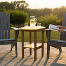 Two Adirondack chairs sit on a patio with the Kanyon Living Poly Lumber Tall Oval Side Table in Yellow and Cedar Wood between them, holding lemon water and glasses. Hands hold an open book; a sunny, green landscape is in the background.