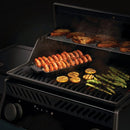 The Napoleon Grills Cast Iron Jumbo Shrimp Tray (67734) sizzles with shrimp skewers, grilled lemon, asparagus, and bread on the upper rack, filling the air with delicious steam.