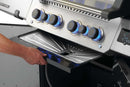 A person slides a Napoleon Grills Drip Pan Liner (3 Pack, 62070) from under a Prestige 500V gas grill, making cleanup of the stainless steel grill with blue-lit knobs quick and easy.