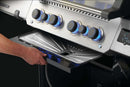 A hand removes a Napoleon Drip Pan Liner (3 Pack, 62070) from under the control knobs of a stainless steel Napoleon Grills Prestige 500V, featuring blue LED dials and easy cleanup with disposable liners.