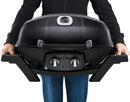 A person holds the Napoleon TravelQ PRO285 Portable Gas Grill by Napoleon Grills, featuring side handles, two control knobs, and a lid-mounted temperature gauge, while wearing a black jacket and blue jeans.