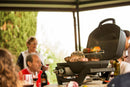 Friends gather outdoors under a shaded canopy, grilling meat and vegetables on the Napoleon Grills TravelQ PRO285 Portable Gas Grill (PRO285-BK), with wine bottles and glasses on the table for a relaxing meal.