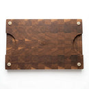 The Two Acre Woodworks Pig Cuts Cutting Board (18.5"x12"x2") features a checkered end grain design, rounded corners, dual half-circle hand grips, and four beige non-slip feet—ideal for BBQ prep.