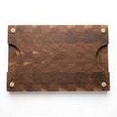 Introducing the Pig Cuts Cutting Board 18"x12"x2" from Two Acre Woodworks—a rectangular end grain board with a checkered grain pattern, rounded corners, convenient side handles, and four white non-slip pads underneath for stability. Ideal for BBQ prep, it features a center-engraved logo.