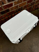 The Polar Bear Coolers Polar Bear 20 Hard Cooler, featuring molded handles, cup holders, and a built-in lid ruler for superior ice retention, sits on wet concrete against a red brick wall.
