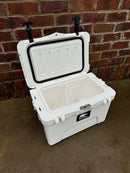 The Polar Bear 20 Hard Cooler by Polar Bear Coolers, featuring two compartments and an open lid, sits on a concrete surface before a red brick wall—ready to deliver superior ice retention for any adventure.