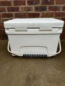 The Polar Bear 20 Hard Cooler by Polar Bear Coolers, featuring a black and white handle, sits on a concrete surface in front of a red brick wall, ready to provide dependable ice retention.