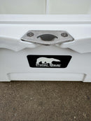 Close-up of a Polar Bear 20 Hard Cooler by Polar Bear Coolers with a metal latch and black label featuring a white polar bear silhouette, resting on concrete.