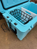 A Polar Bear Coolers 45 Hard Cooler in light blue sits on concrete with its lid open, revealing a black wire basket and divider. This rugged cooler offers extended ice retention and has a black metal cup holder on the front.