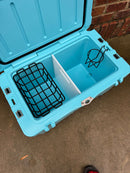 A blue Polar Bear Coolers 45 Hard Cooler sits on concrete by a brick wall, lid open to reveal a black wire basket, white divider, and black wire cup holder inside this rugged cooler designed for extended ice retention.