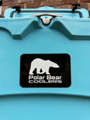 Close-up of the Polar Bear Coolers 45 Hard Cooler, featuring a black-and-white polar bear logo on the front. A brick wall is in the background. Built by Polar Bear Coolers for extended ice retention in rugged outdoor settings.