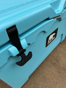 Close-up of a Polar Bear Coolers 45 Hard Cooler in light blue with a black latch and white bear logo, set on concrete. This rugged outdoor cooler is designed for superior ice retention and durability.