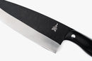 A close-up of the Folded Steel Primrose 8 Inch Chef Knife, showcasing its 1095 high-carbon steel black blade and handle with a silver logo near the bolster, set against a white background.
