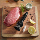 A raw steak rests on a wooden cutting board, surrounded by the Amazon Round 24-Blade Meat Tenderizer, a marinade tool, cleaning brush, lemon halves, salt, peppercorns, and fresh herbs.